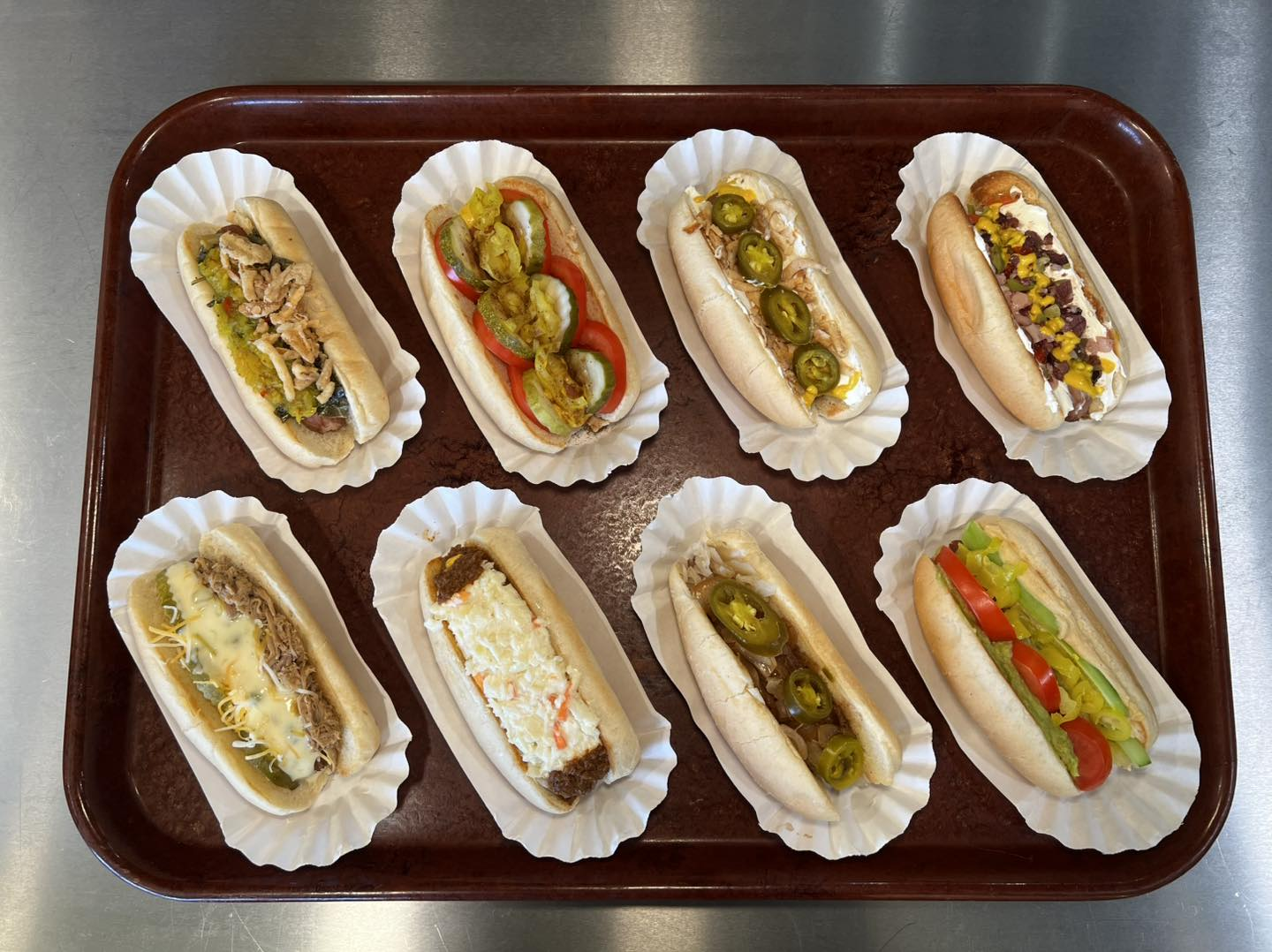 Actual Franken Dogs tray with eight hotdogs topped with tomatoes, peppers, pickles, chili, cheese, slaw, and onions